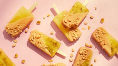 several popsicles with peanut butter on them sitting on a pink surface, one is cut in half and the other two are filled with peanuts