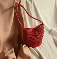 a red crocheted purse sitting on top of a white bed sheet with pillows