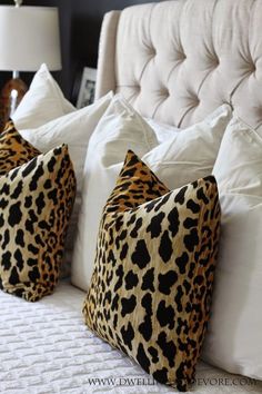 two leopard print pillows sitting on top of a bed next to white sheets and pillows