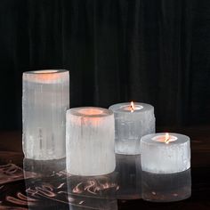 three white candles sitting next to each other on top of a wooden table covered in ice