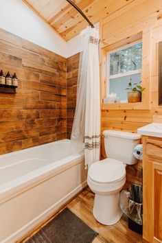 a white toilet sitting next to a bath tub in a bathroom under a wooden ceiling