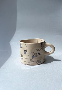 a white cup with blue leaves on it is sitting on a gray surface and has a shadow from the wall behind it