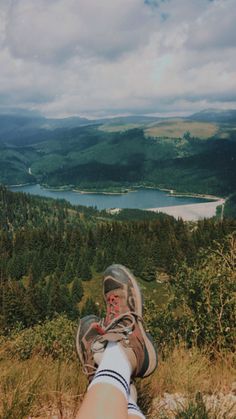 a person with their feet in the air on top of a hill overlooking a lake