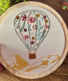 a hand is holding a embroidery kit with a hot air balloon in the sky on it