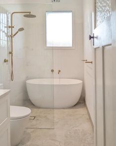 a white bath tub sitting next to a toilet under a window