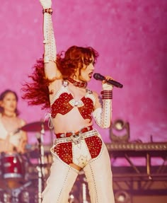 a woman in white and red outfit on stage with her hands up to the air