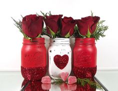 three mason jars with red roses in them and one has a heart painted on it