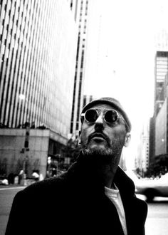 a man wearing sunglasses standing in the middle of a city street with tall buildings behind him