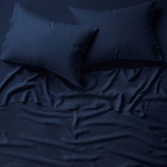 two dark blue pillows on top of a bed with black sheets and pillowcases