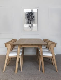 a wooden table with white chairs in front of a painting on the wall above it