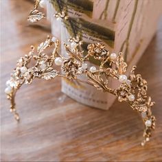 a gold tiara with pearls and leaves on top of a wooden table next to a book