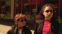 two children wearing sunglasses and bow ties walking down the street