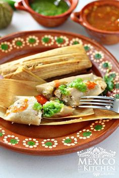 two tamales on a plate with sauces and condiments