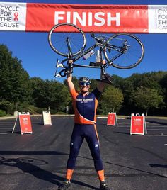 a man is holding up his bike over his head while standing in front of a finish line