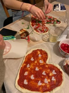 a woman making heart shaped pizzas on top of a table with other food items