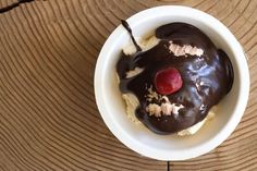 an ice cream sundae with chocolate and cherries in a white bowl on a wooden table