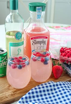 two glasses filled with pink lemonade and raspberries next to bottles of simply light