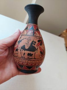 a hand holding a small vase with designs on it's sides and an animal painted on the side