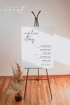 a white sign sitting on top of a wooden floor next to a vase filled with flowers