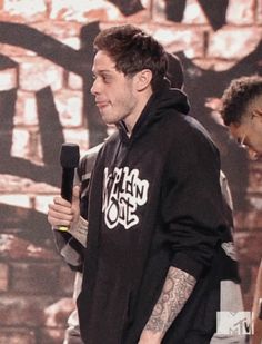 a man in a black hoodie holding a microphone and standing next to another man