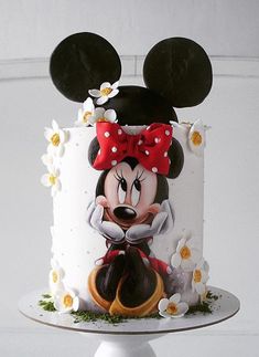 a mickey mouse cake is decorated with flowers and daisies on a white pedestal in front of a white wall