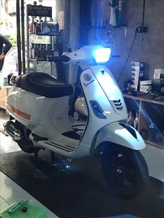 a scooter parked in a garage with its lights on and people working behind it