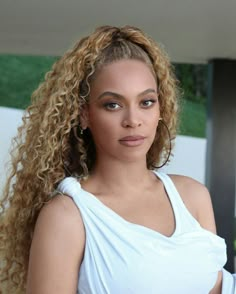 a close up of a person wearing a white shirt and long curly hair with an afro