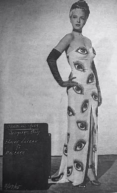 a woman in a dress with an eye pattern on it, standing next to a sign