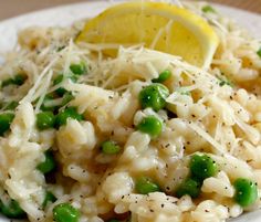 a white plate topped with rice and peas covered in grated cheese next to a lemon wedge