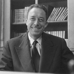 a black and white photo of a man in a suit smiling at the camera with bookshelves behind him