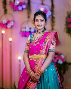 a woman in a pink and blue sari standing next to a wall with candles