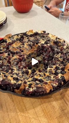 a blueberry pie sitting on top of a wooden table next to plates and bowls