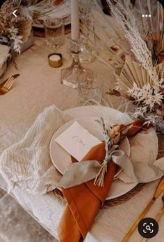 the table is set with white plates and napkins, gold candlesticks, and dried flowers