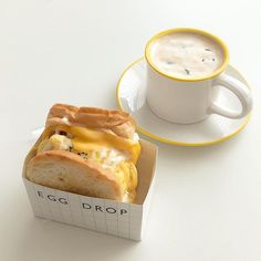 an egg and cheese sandwich in a box next to a cup of cappuccino