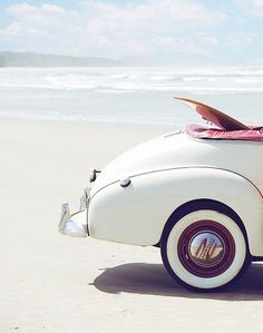 an old car parked on the beach with surfboards sticking out of it's hood