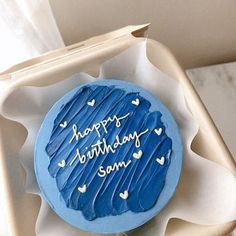 a blue frosted birthday cake sitting in a box on top of a white table