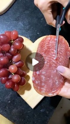 a person cutting up a piece of meat next to grapes on a heart shaped board