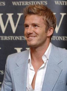 a man in a gray suit smiling at the camera with watertones wall behind him