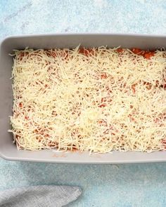 a casserole dish with cheese and tomato sauce on the side, ready to be baked