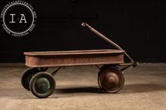 an old fashioned wooden wagon with wheels on the floor in front of a brick wall