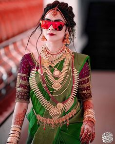 a woman in a green and red sari with jewelry on her face, wearing sunglasses