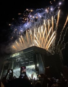 fireworks are lit up in the night sky above a stage with people standing on it