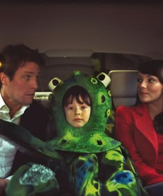 a man and woman sitting in a car with a child dressed up as a frog