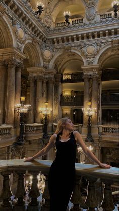 a woman in a black dress is standing on a balcony with chandeliers and lights