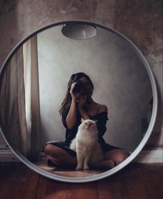 a woman sitting on the floor in front of a mirror with a cat looking at her reflection