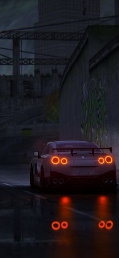 a red sports car driving down a wet road at night with its headlights turned on