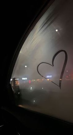 there is a heart drawn on the side of a car window with city lights in the background