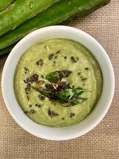 a white bowl filled with green soup next to some asparagus on a table