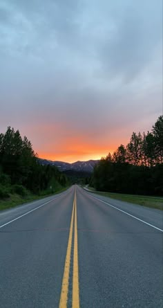 the sun is setting on an empty road with mountains in the background