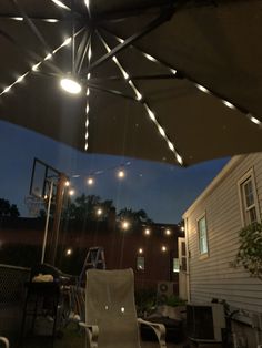 an outdoor patio with lights strung from the ceiling and chairs on the ground, in front of a house